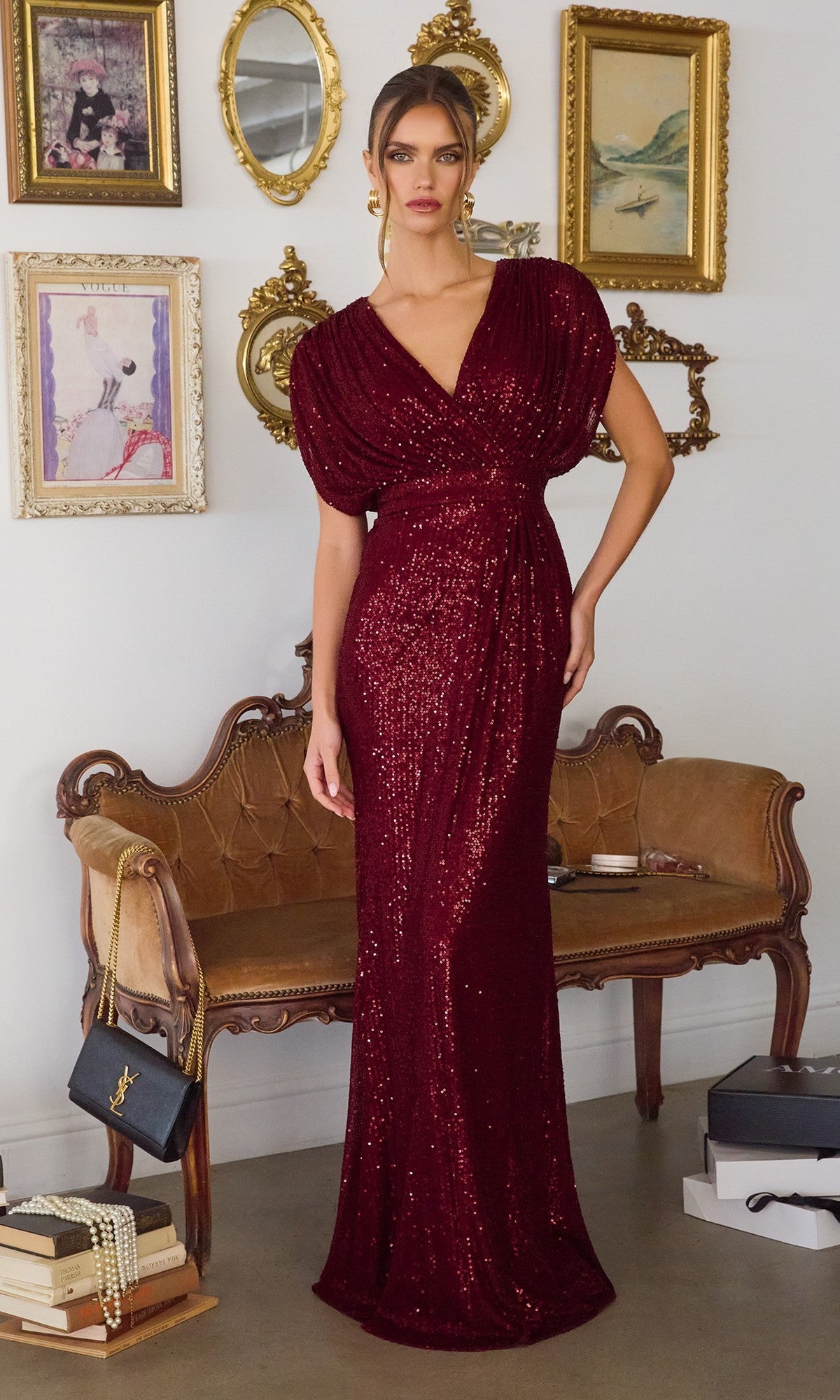 A woman wearing the Cap-Sleeve Long Sequin Formal Dress: Amoris T101 stands before a vintage sofa and ornate framed art on a white wall.